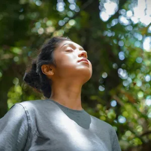 Mujer con los ojos cerrados respirando entre árboles
