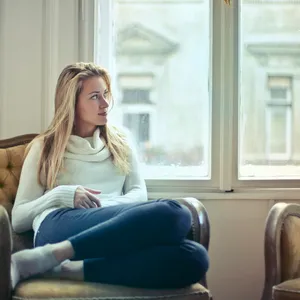Mujer sentada en un sillón junto a la ventana, pensativa